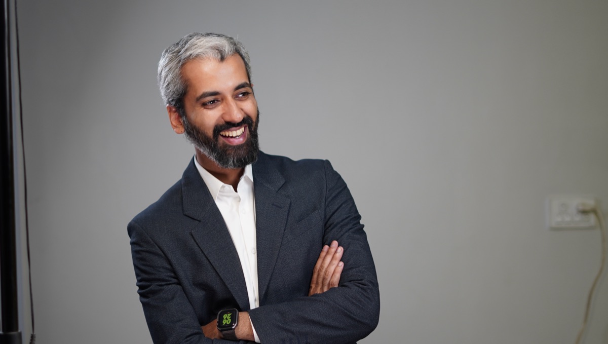 Sameer Ahmed Khan, color studio portrait, navy blazer and white shirt, laughing